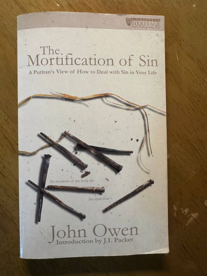 木のテーブルに置かれた洋書のペーパーバック。表紙には錆びた釘が散らばった写真と『The Mortification of Sin ― A Puritan's View of How to Deal with Sin in Your Life』、著者 John Owen、Introduction by J.I. Packer と印刷されている