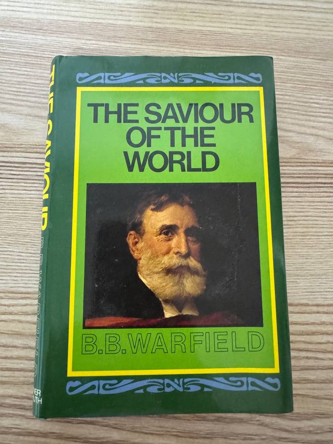 木のテーブルに置かれたB・B・ウォーフィールド『THE SAVIOUR OF THE WORLD』の緑色のハードカバー。中央に白い顎ひげの男性の肖像画が入っている
